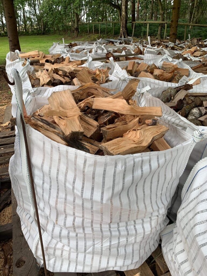 A bulk bag of pale, irregularly split softwood logs